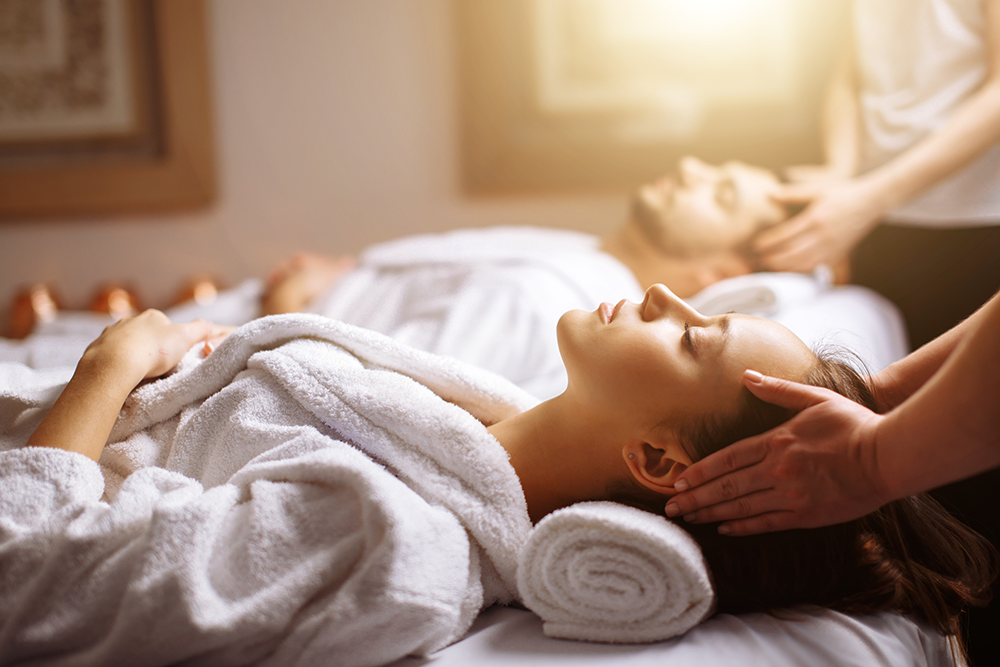 Couple in robes laying on massage table getting a facial massage in spa