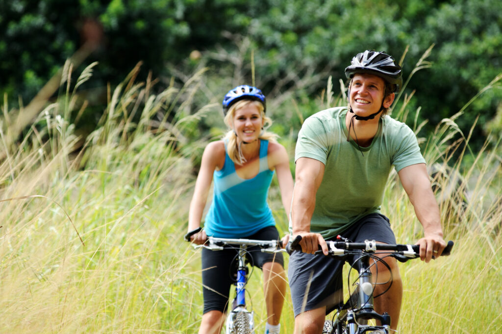 A happy couple rides their bike through a field.