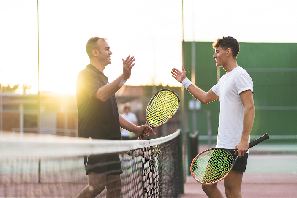 A father and son shake hands over a tennis net