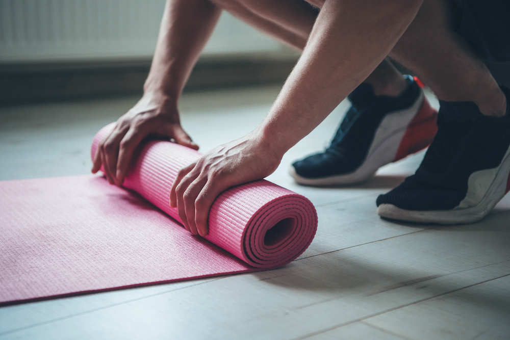 A man rolling up his yoga mat after class