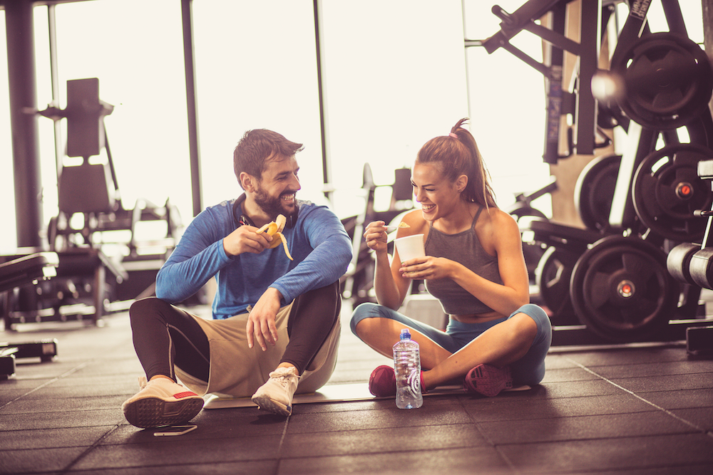 A fit couple enjoy a snack together at the gym