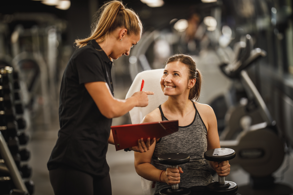 A personal trainer helps coach a young woman at the gym
