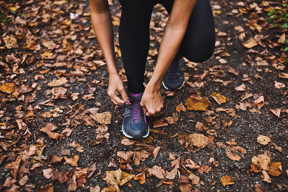 A woman laces up her shoes to go running outdoors