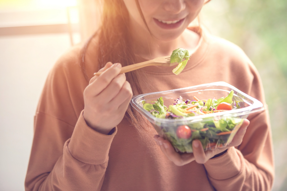 A close up of a young woman eating a salad