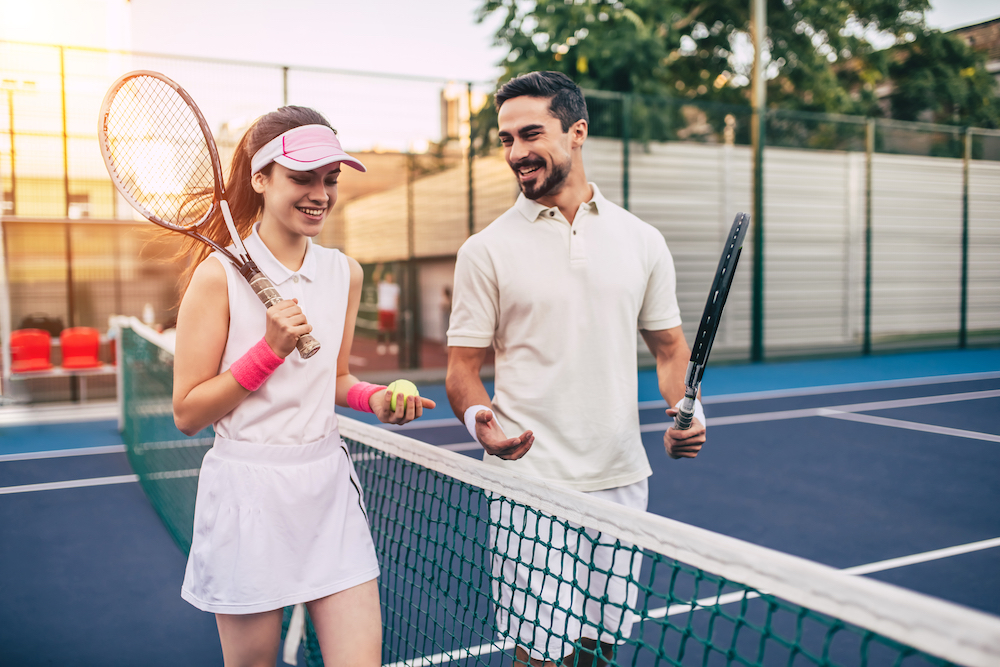 Two friends holding tennis rackets talk after playing a match