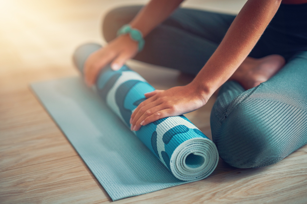 A woman sitting cross legged and rolling up her yoga mat