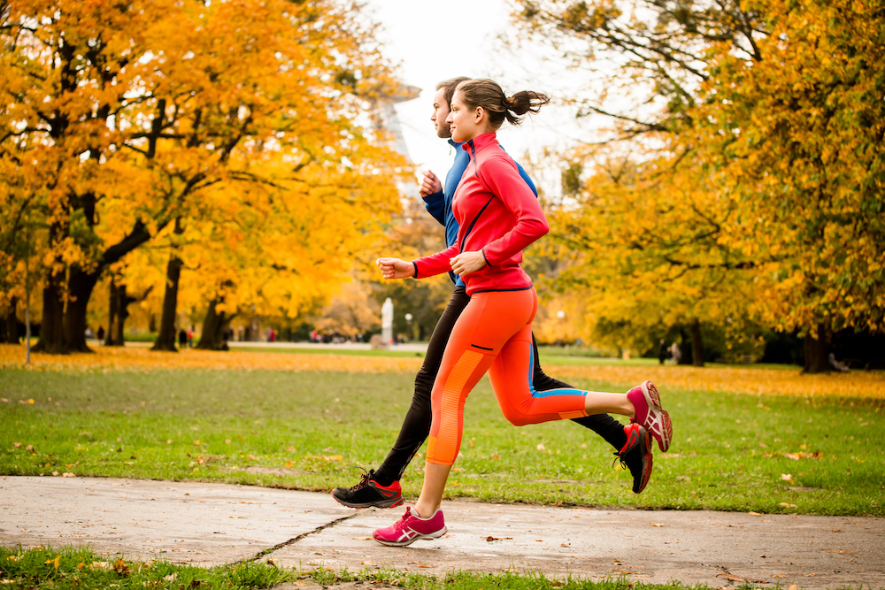 A young couple jogging in a park outdoors during the fall wealther