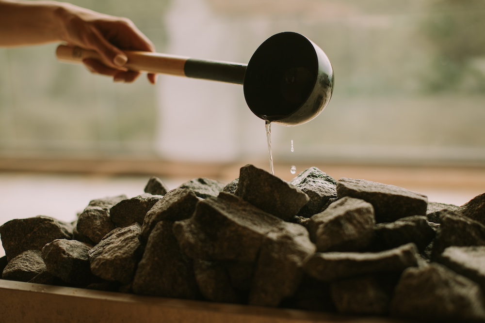 A young woman's hand pouring water on hot rocks in the sauna