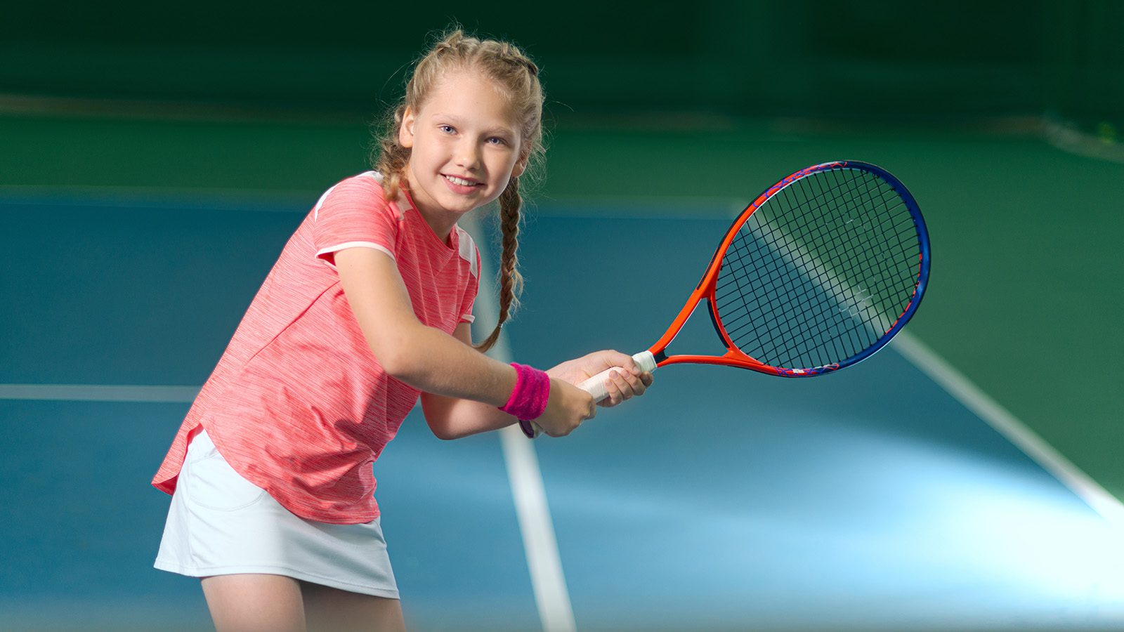 A girl plays tennis on an indoor tennis court.